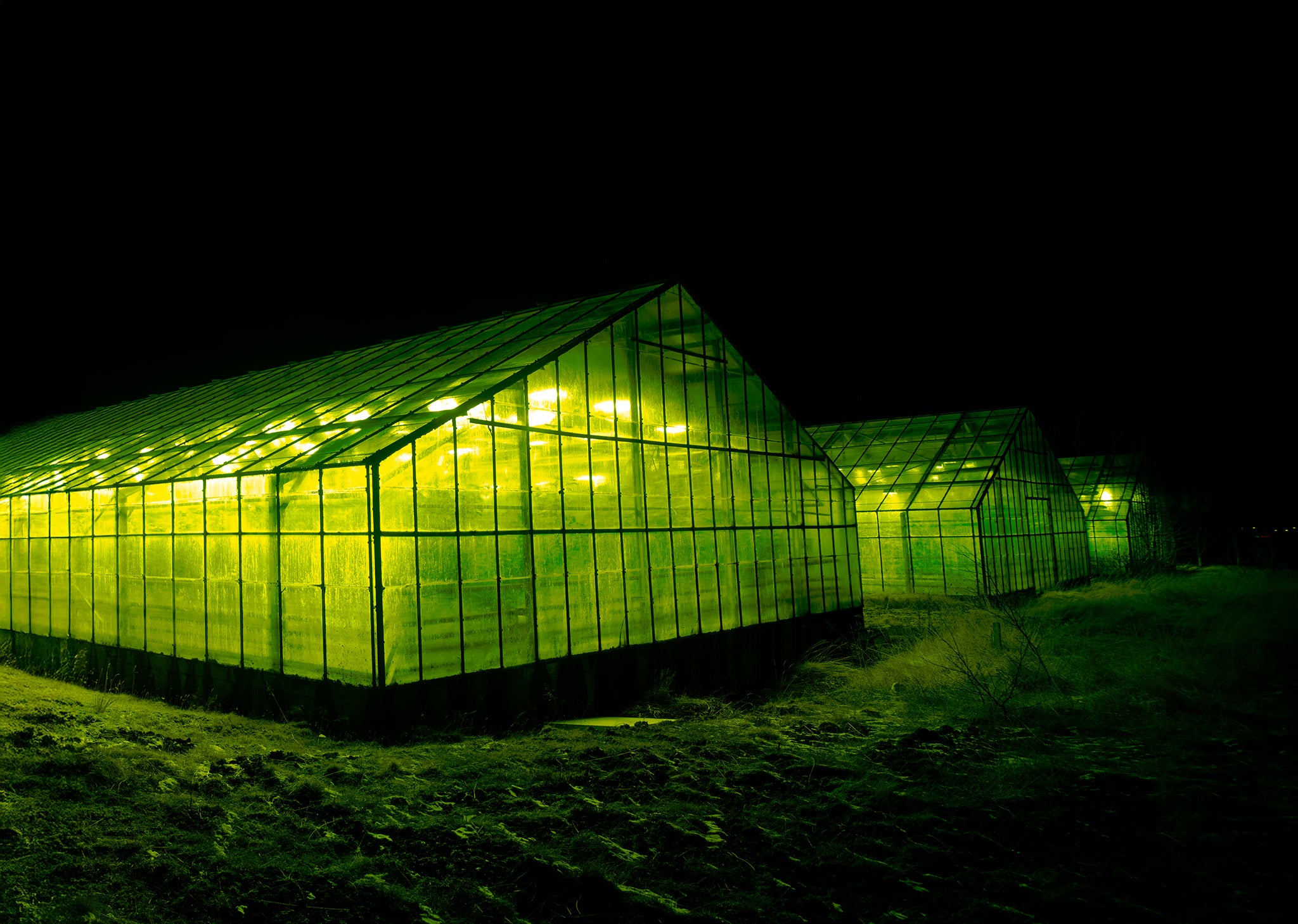Glowing green greenhouse at night in Iceland, surreal beacon of light in dark landscape, fine art photograph